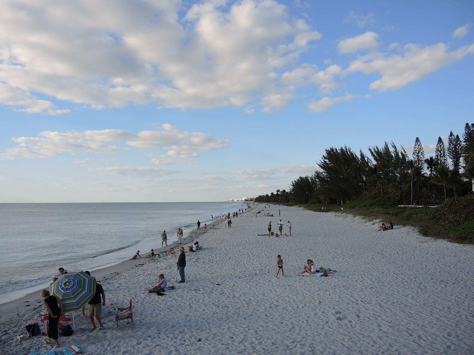 9th Avenue South Beach: sandy beach with scattered visitors, calm water, trees, cloudy sky