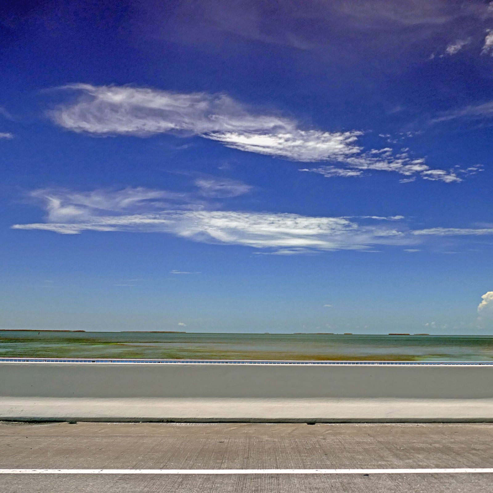 Anne's Beach: sandy beach with shallow water, seawall, blue sky and white clouds