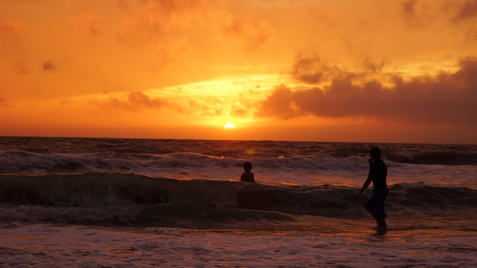 Bayview Avenue Beach: sunset over ocean with silhouetted surfers in water