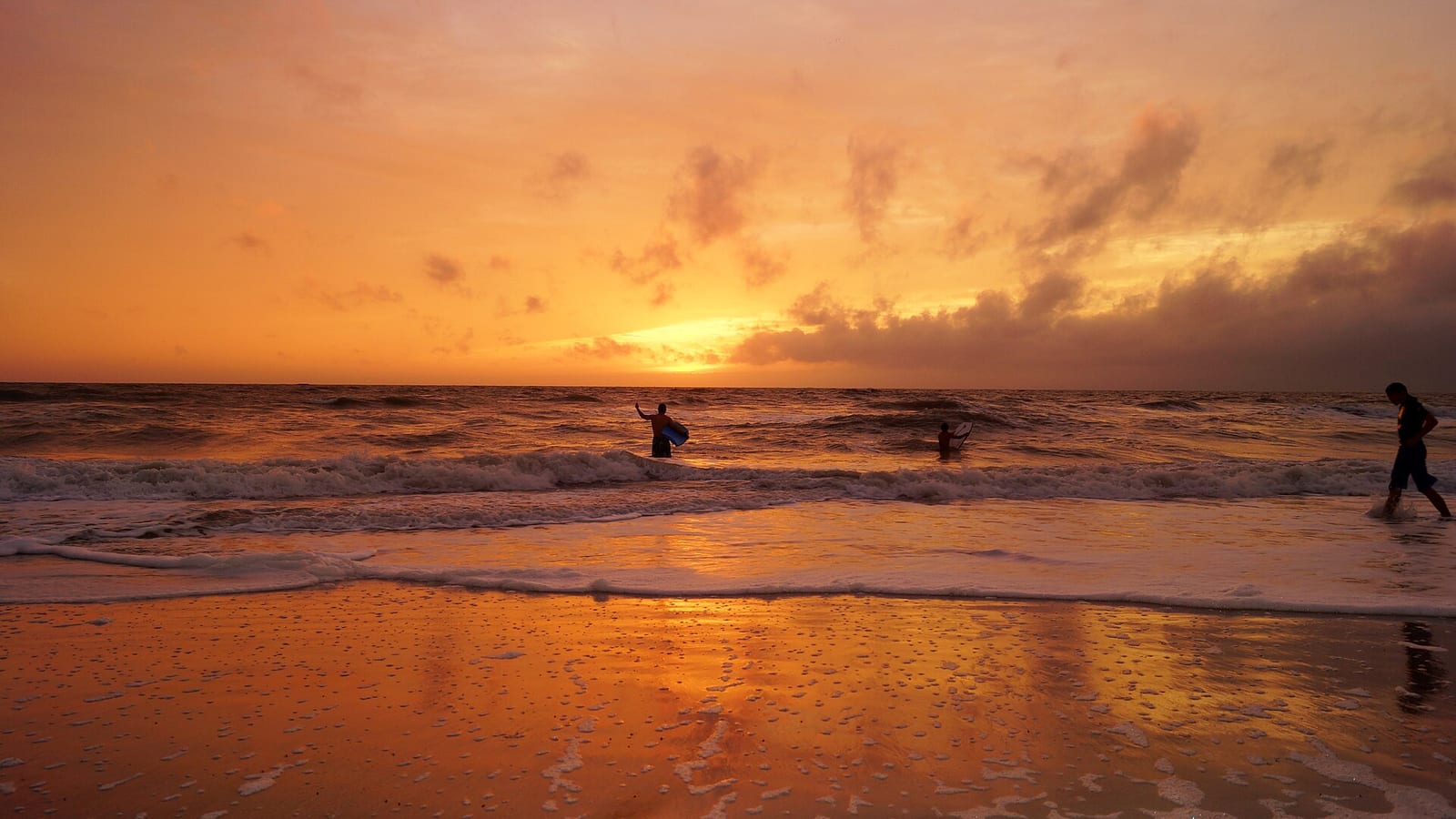 Bayview Avenue Beach: sunset over ocean with silhouetted surfers in water and on beach