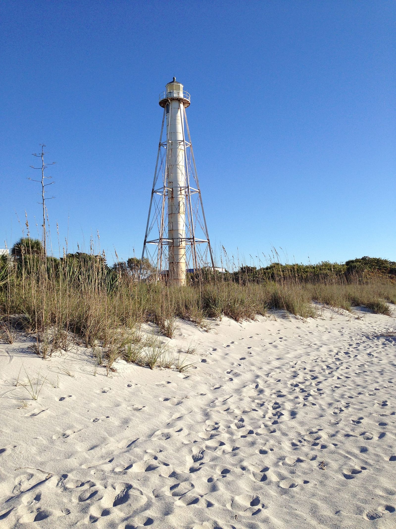 Boca Beach: lighthouse on sandy beach with dune grass under clear blue sky