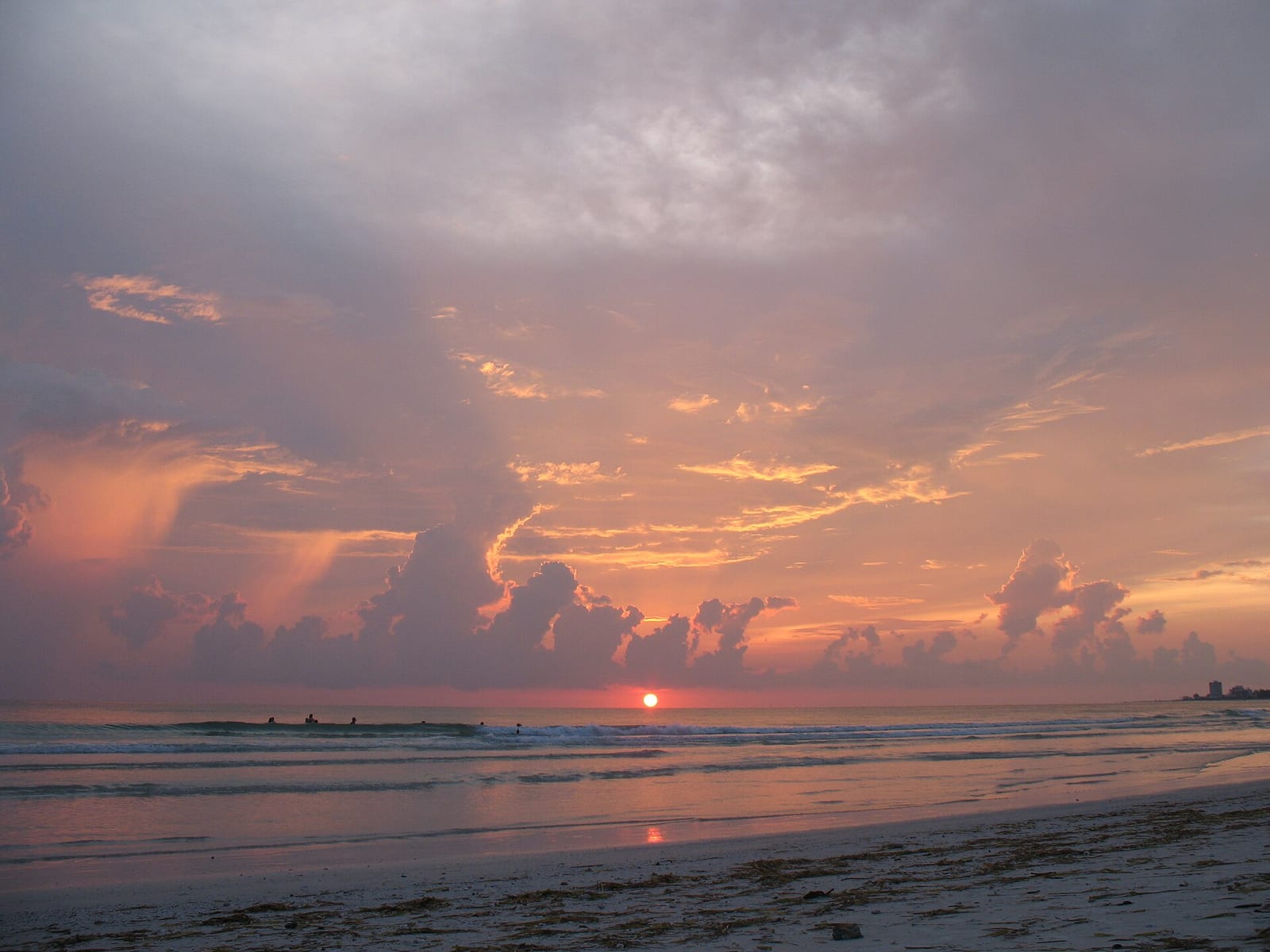 Crescent Beach: sunset over ocean with clouds and distant surfers in water