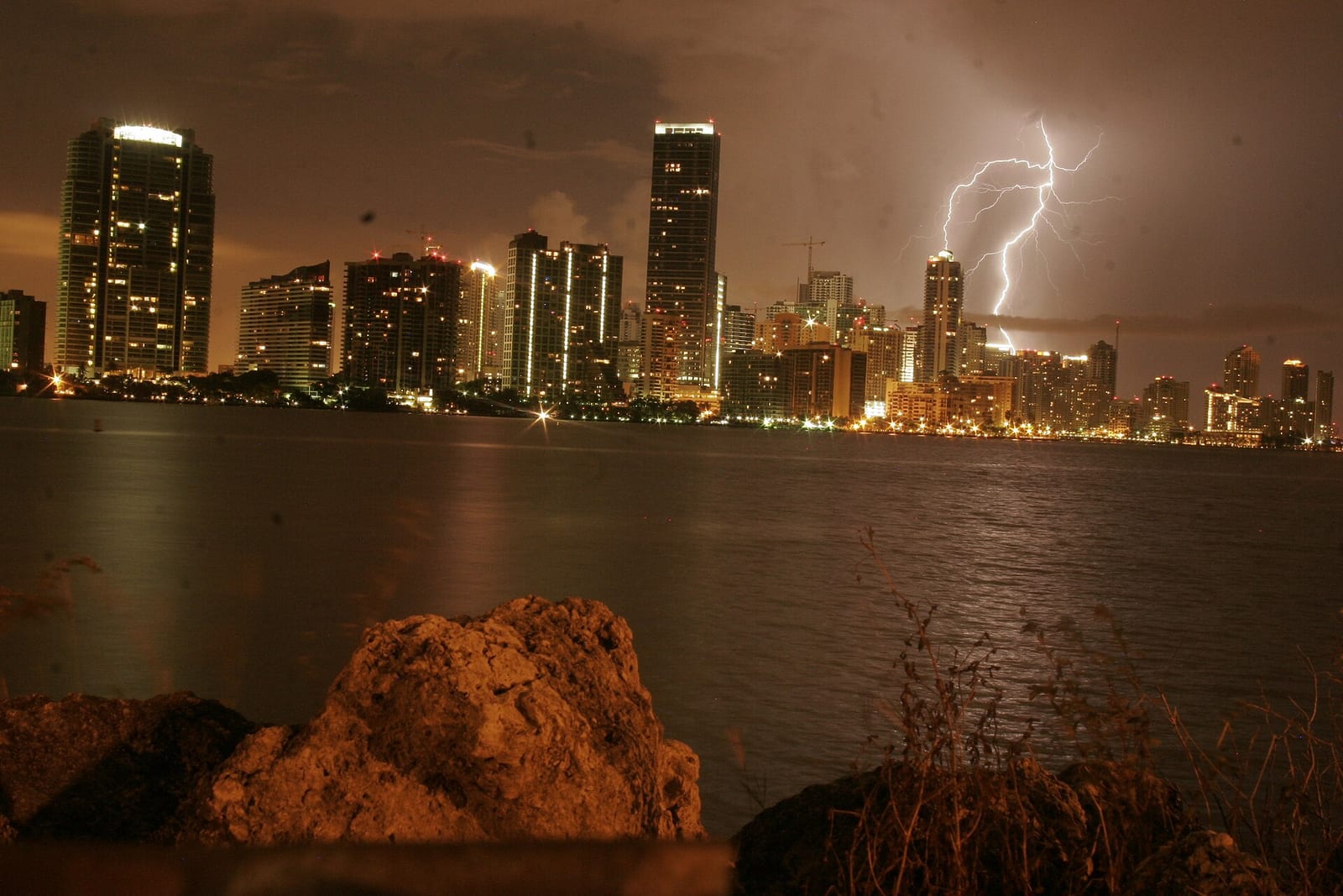 Hobie Island Beach Park: city skyline at night with lightning storm over water and rocks
