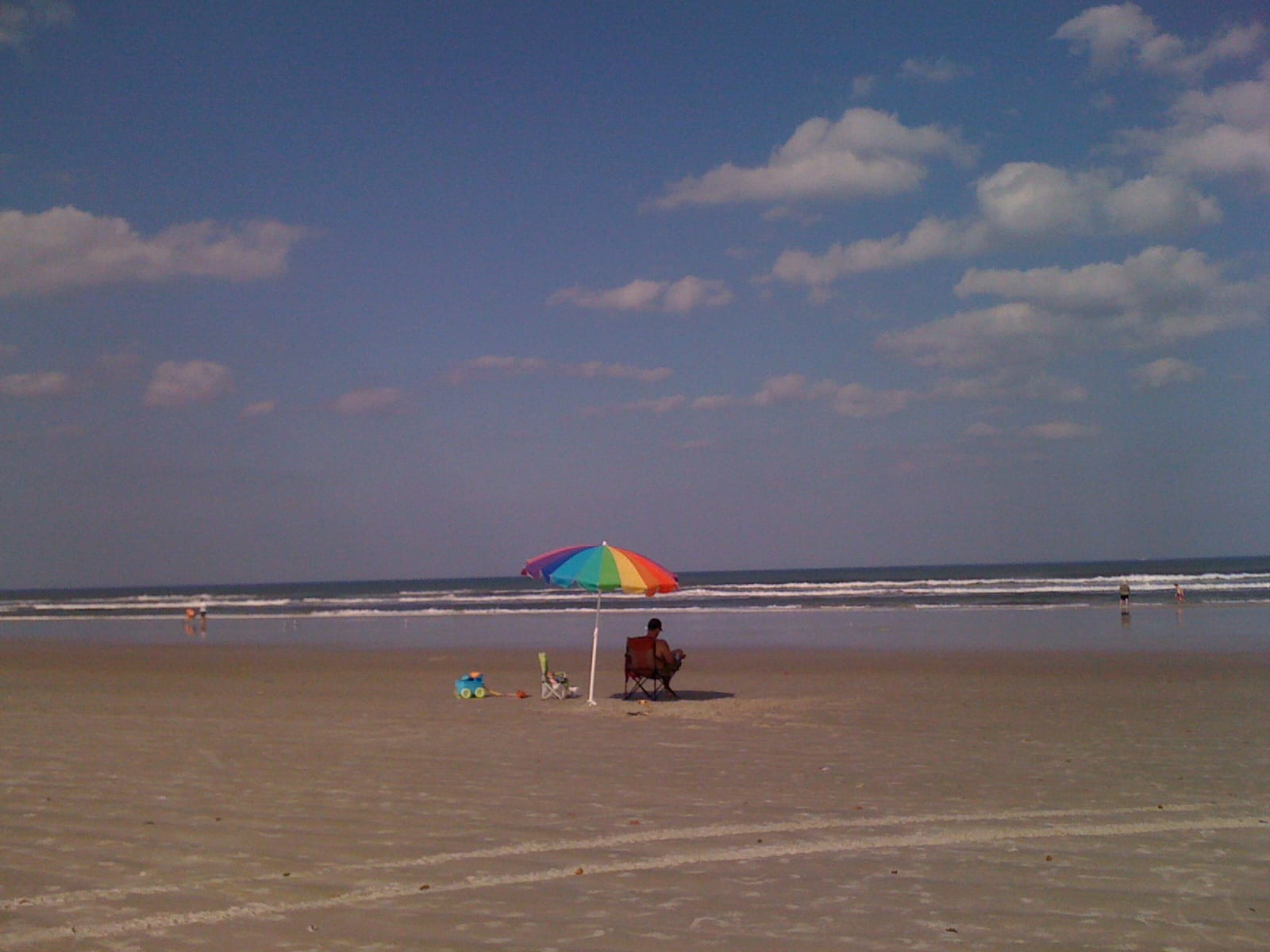 New Smyrna Beach: beach scene with colorful umbrella, beachgoers, ocean, and cloudy sky