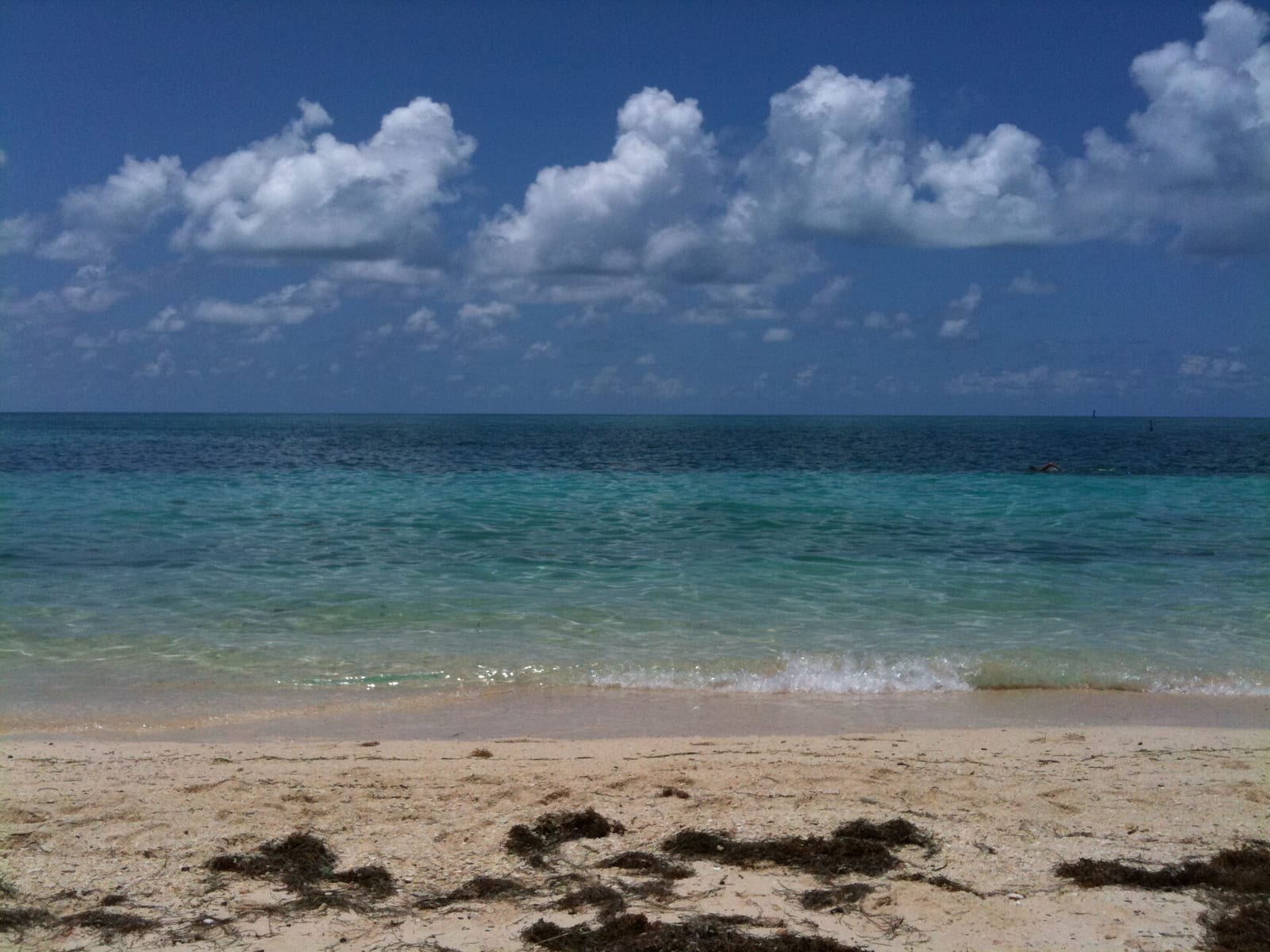 North Swim Beach: sandy beach with turquoise water, waves, and cloudy blue sky