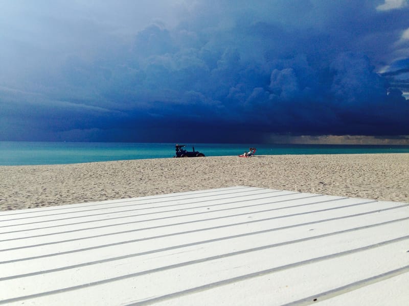 Ocean Terrace Public Beach: beach with wooden deck, turquoise water, dramatic storm clouds, distant vehicles