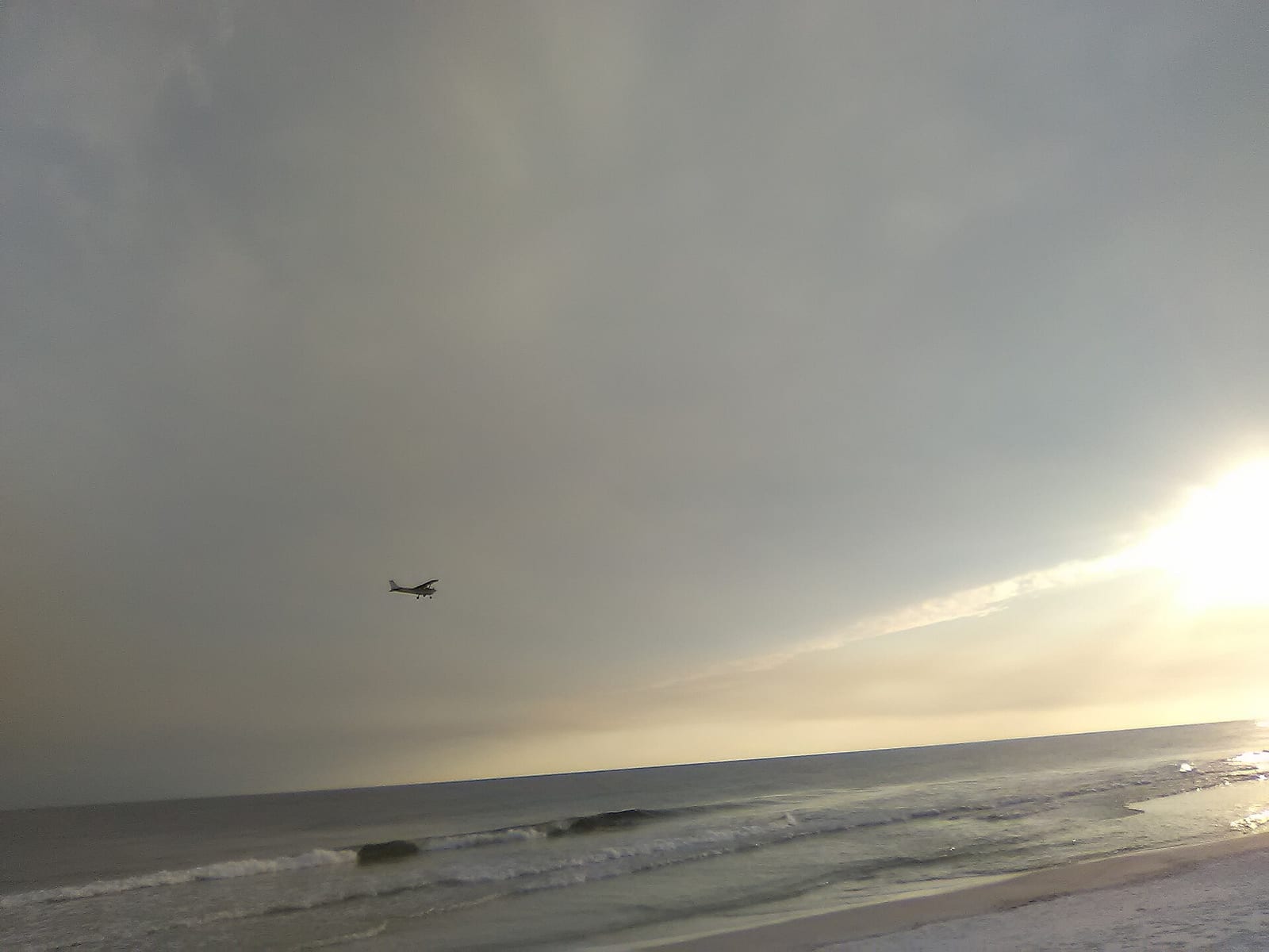 Park West On-Leash Dog Beach: beach shoreline with waves, overcast sky, and aircraft flying overhead