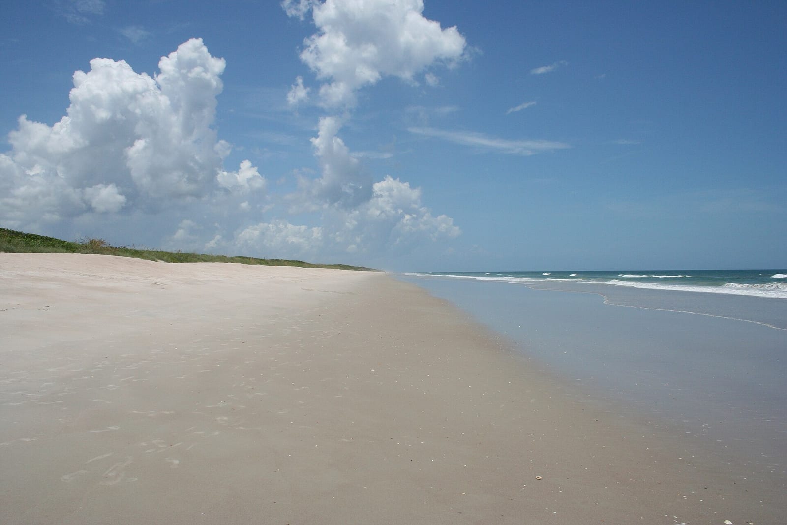 Playalinda Beach (Nudist Area): wide sandy beach with dunes, calm water, and blue sky with clouds
