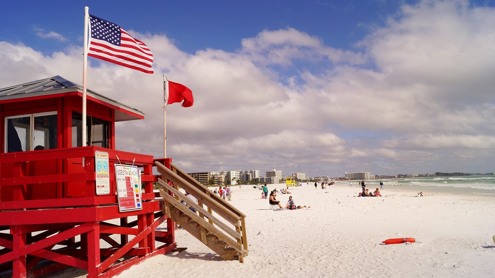 Siesta Beach: red lifeguard tower with flags on sandy beach with swimmers