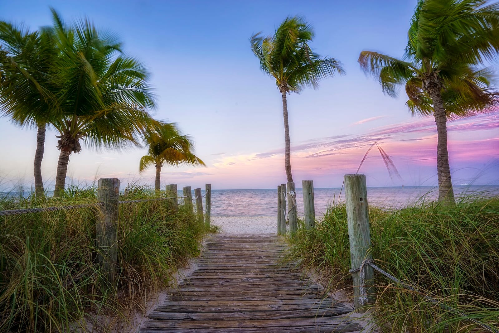 Smathers Beach: wooden boardwalk through dunes with palm trees at sunset
