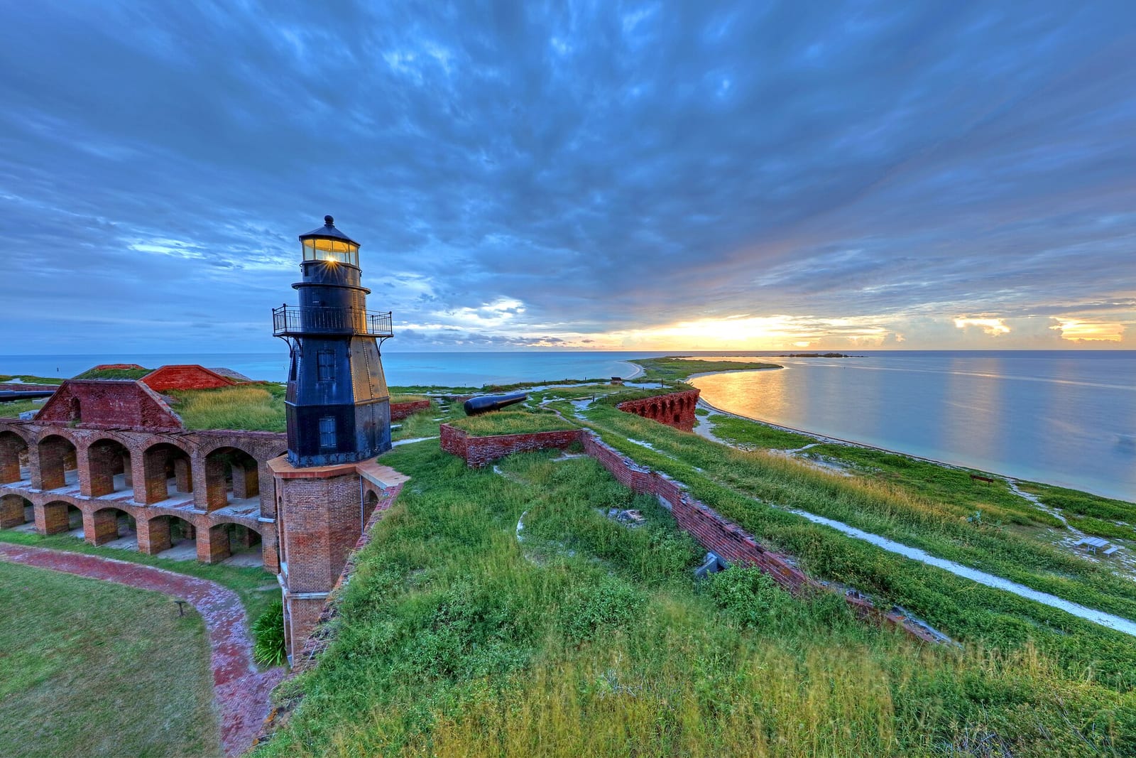 South Swim Beach: lighthouse and fort ruins on grassy coastal point at dusk
