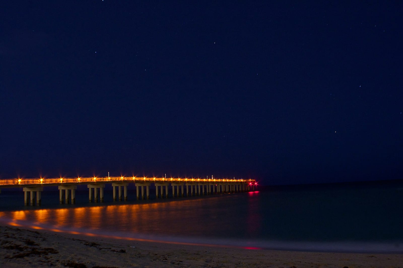 Sunny Isles Beach: illuminated pier extending into dark water at night with beach shore visible