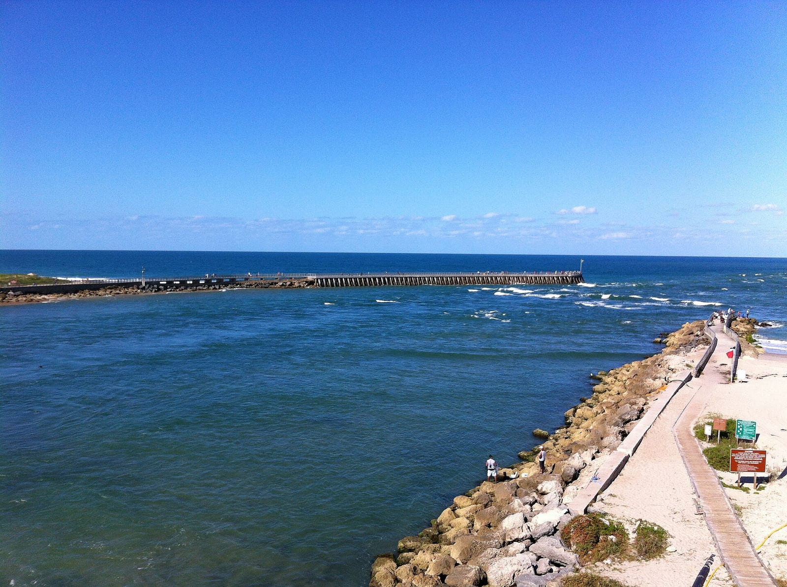 Tidal Cove Beach: coastal pier, rocky shoreline, walkway, ocean horizon with clear sky